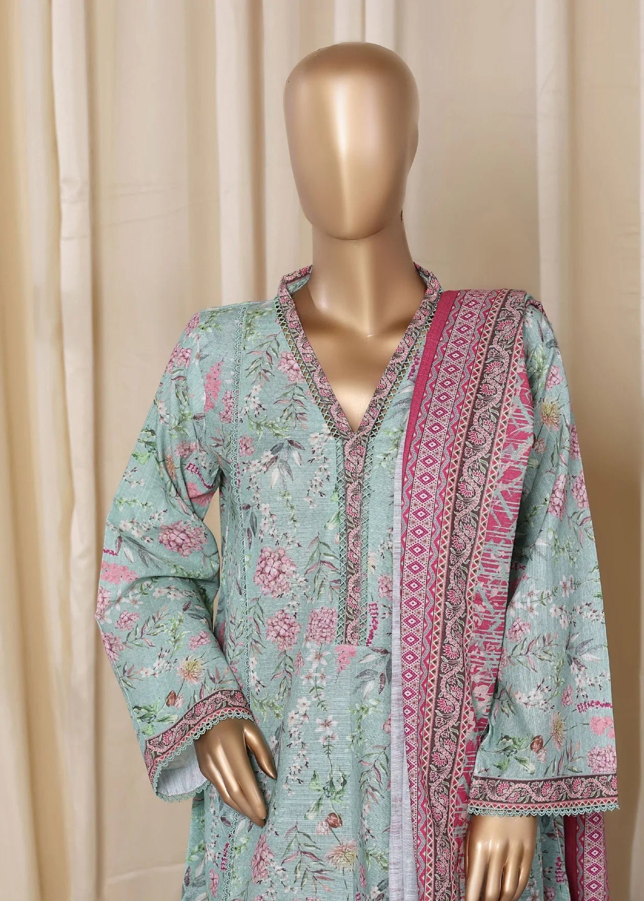 Mannequin wearing a light blue embroidered outfit with pink accents against a beige curtain background.