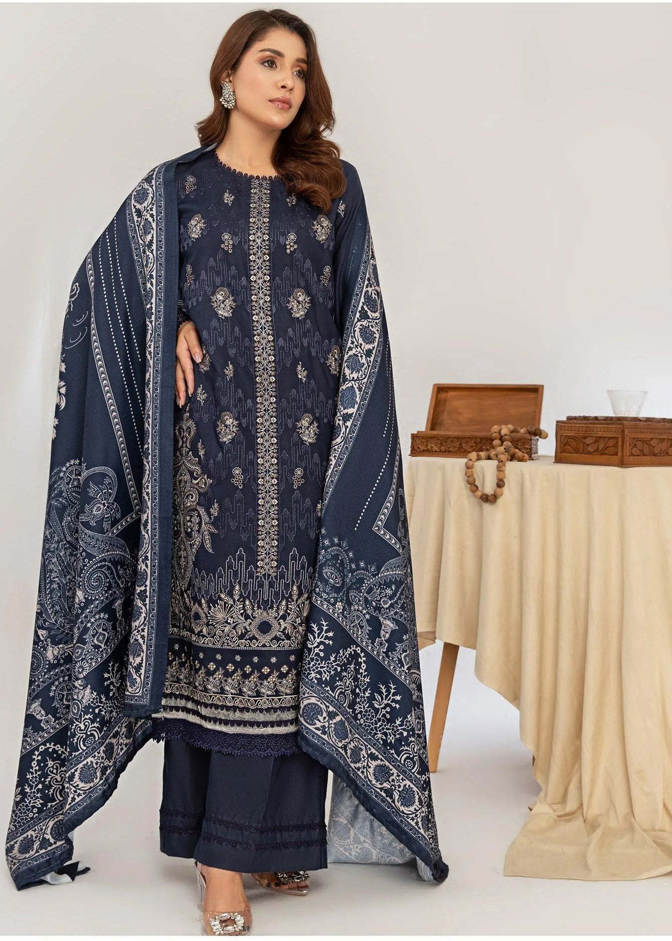 Woman wearing a dark blue embroidered traditional outfit with a beige tablecloth and boxes in the background.
