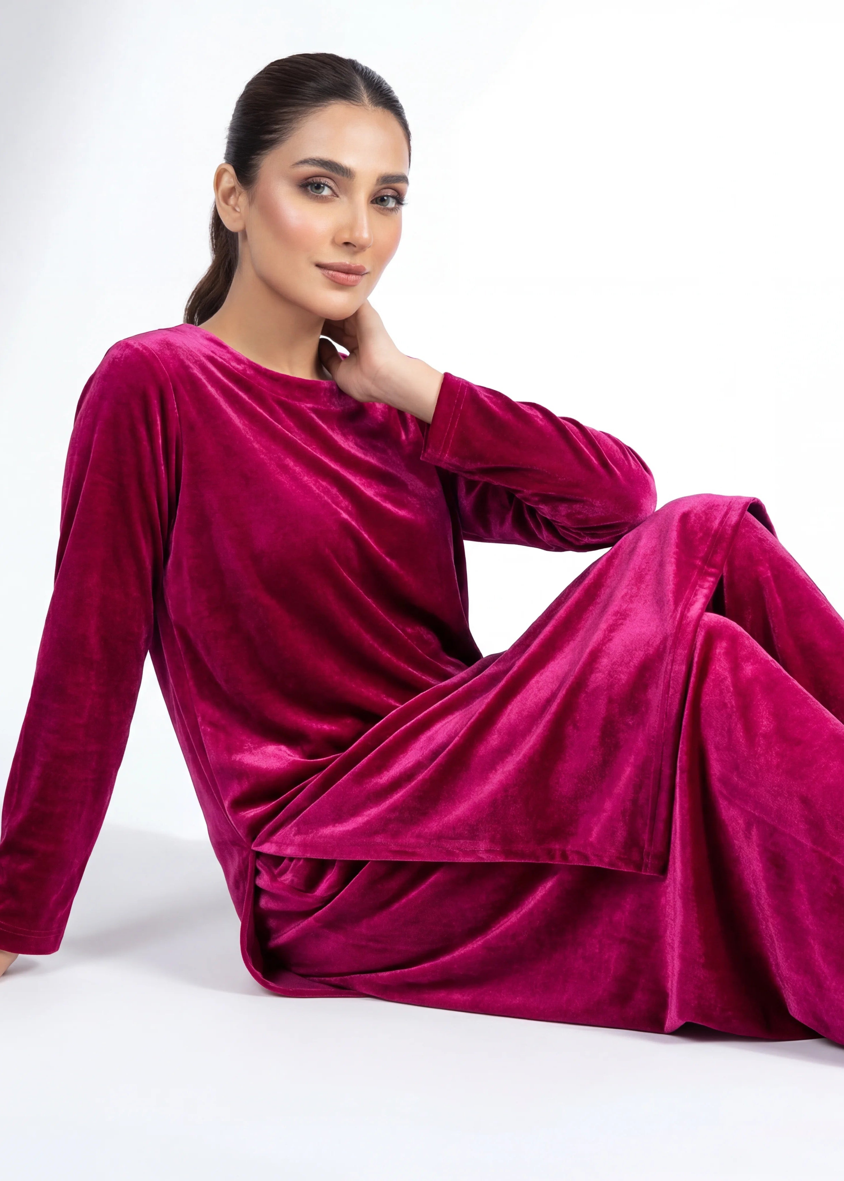 Woman wearing a pink velvet suit sitting on a white background