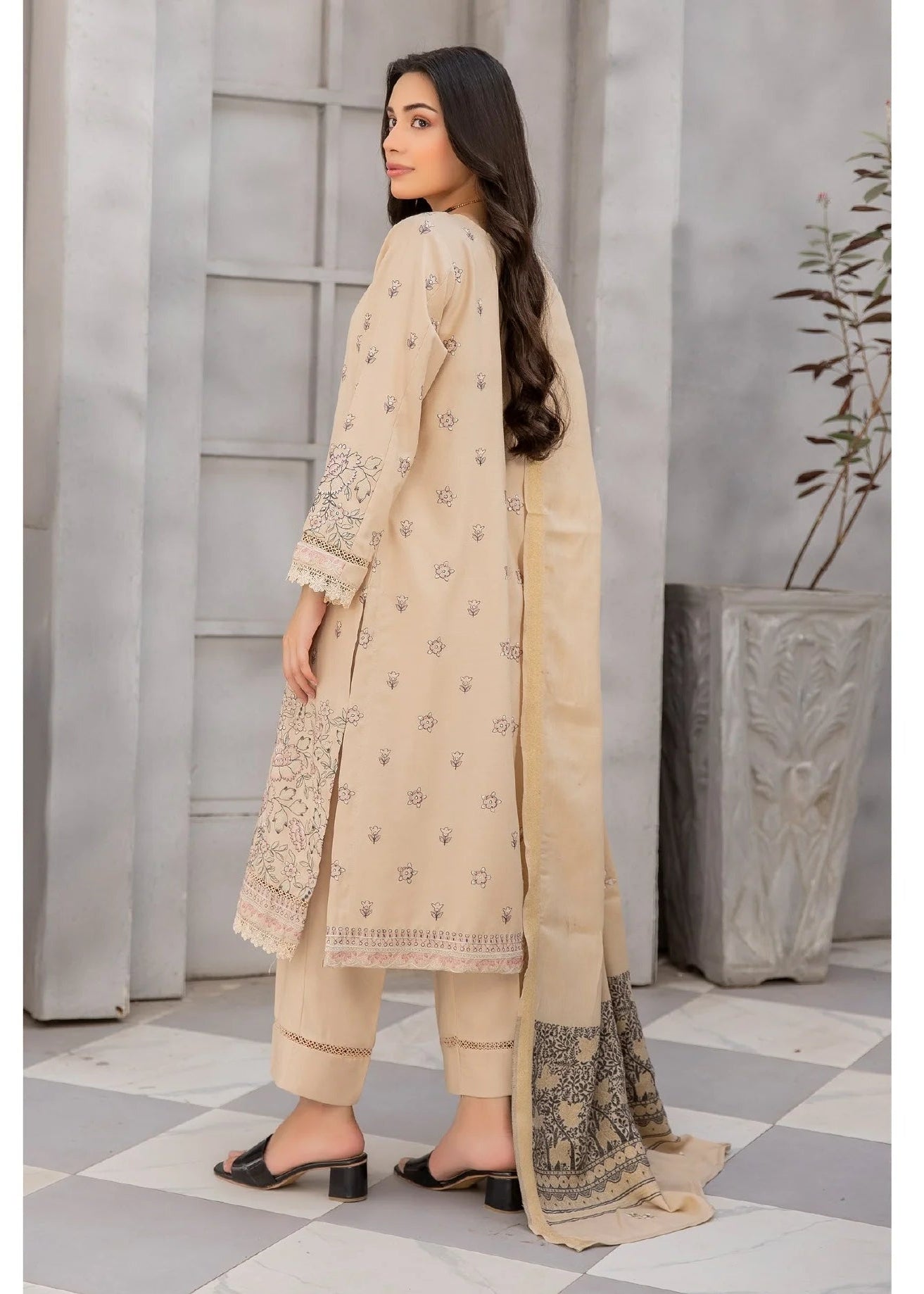 Woman in a beige traditional outfit with floral patterns in an indoor setting.