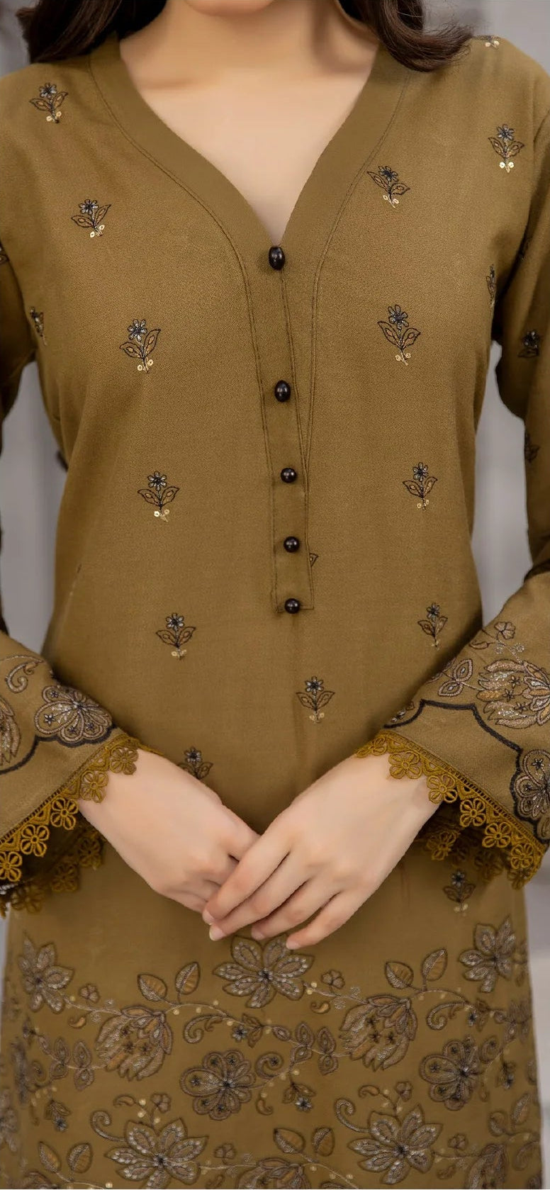 Woman wearing a brown traditional outfit with floral patterns, standing indoors.