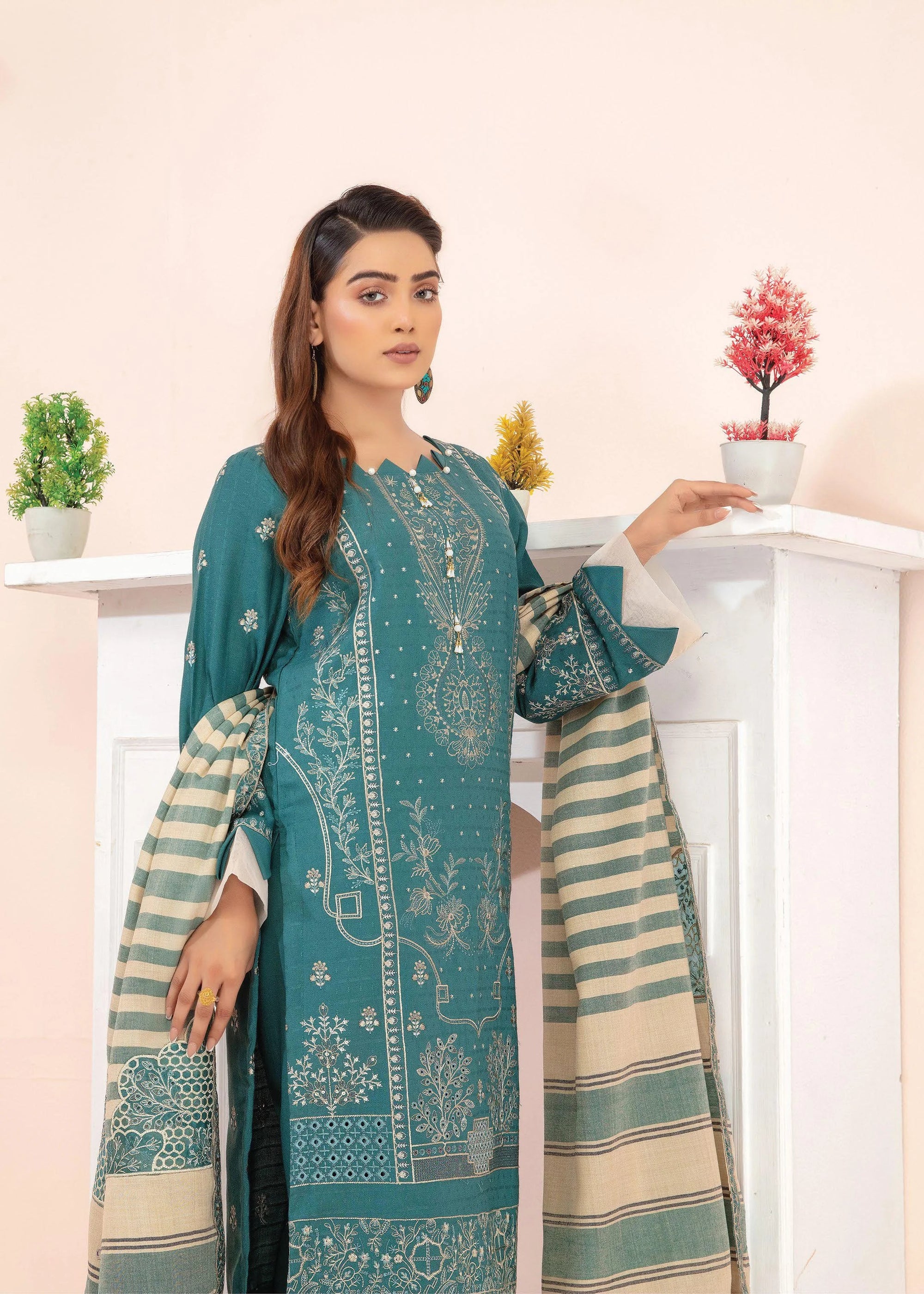 Woman wearing a teal embroidered outfit with decorative elements on a light pink background