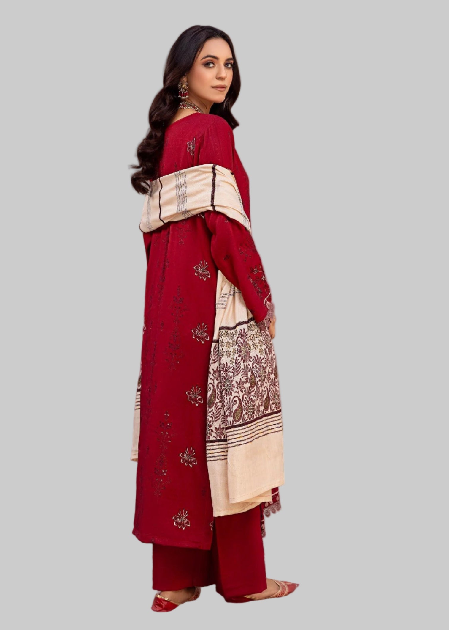 Woman in a red traditional outfit with beige patterns in a decorated room.