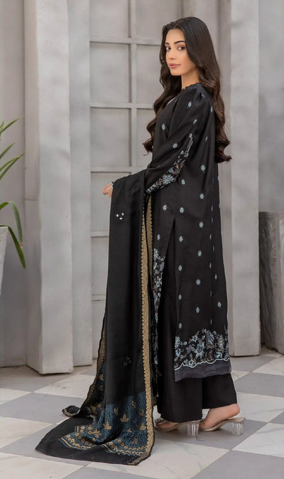 Woman in a black traditional outfit with floral patterns standing in a room with gray walls and a checkered floor.