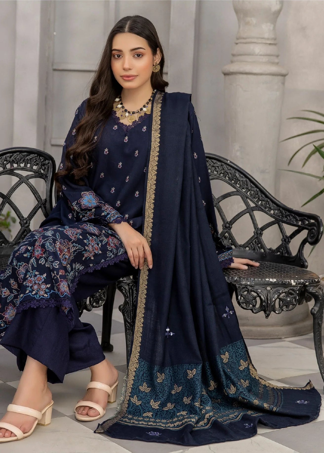 Woman in a navy blue traditional outfit sitting on a bench in an elegant indoor setting.