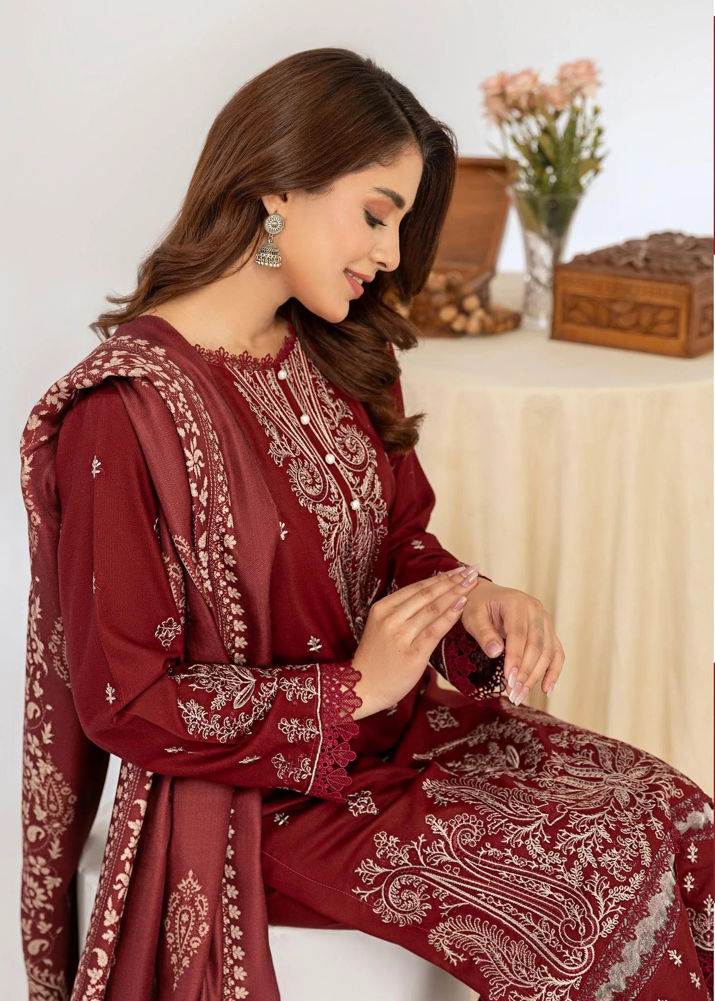 Woman wearing a maroon embroidered outfit with close-up details on a white background