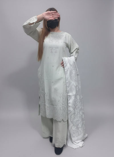 A Women wearing a light-colored embroidered outfit against a green background