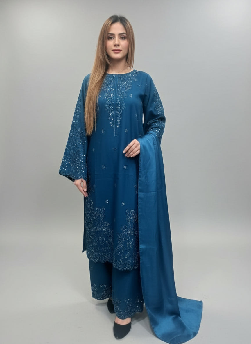 A Girl wearing a blue embroidered outfit with a green textured wall in the background