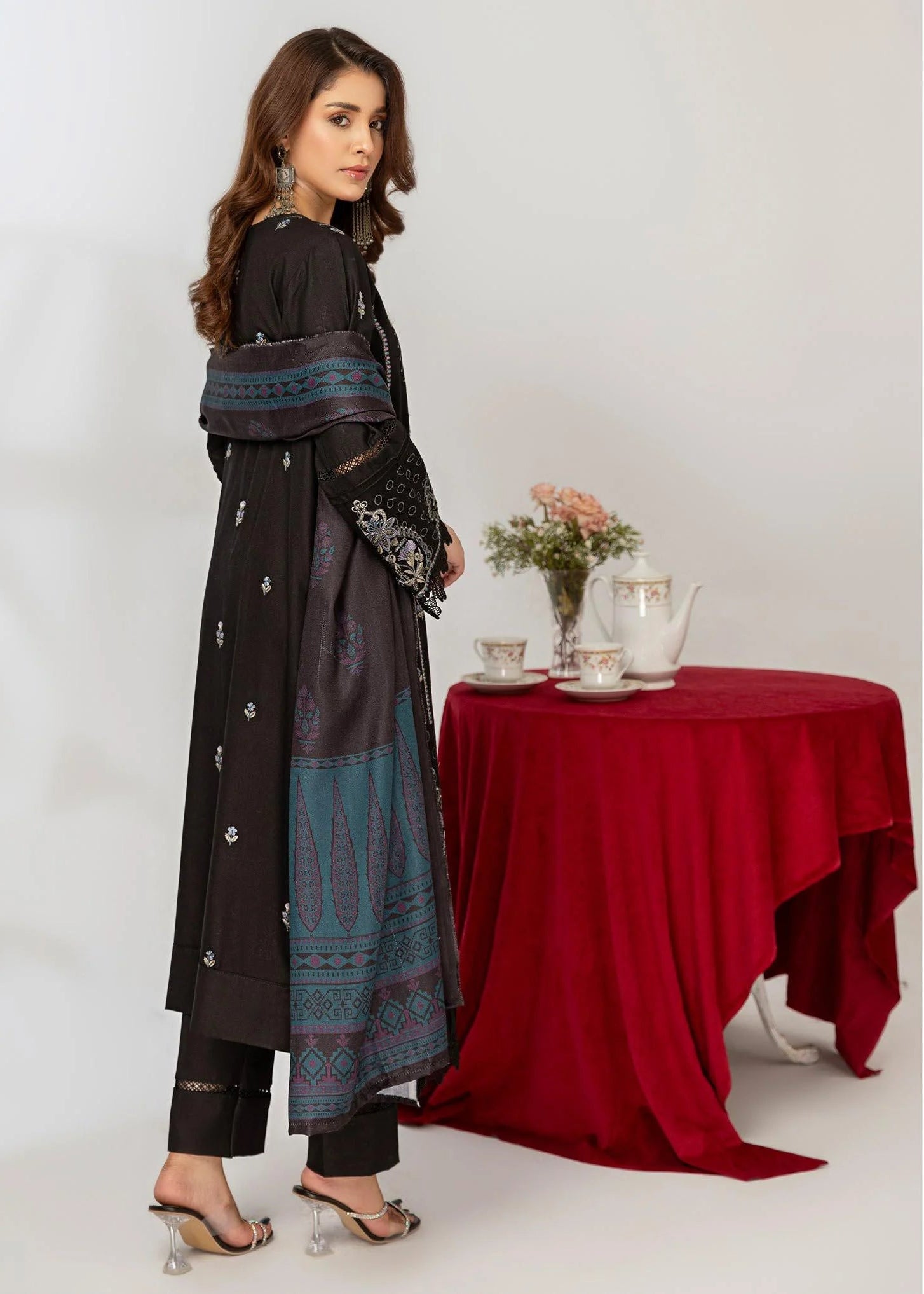 Woman in a black traditional outfit standing next to a table with a red tablecloth.