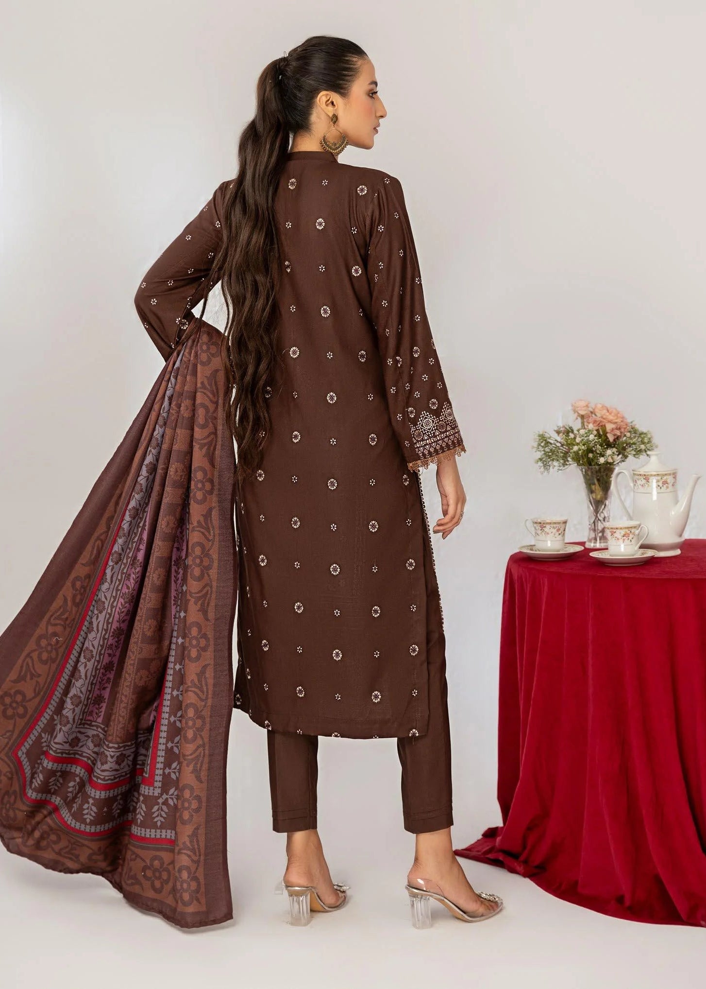 Woman in a brown traditional outfit with a matching dupatta, posing in front of a table with a red tablecloth.