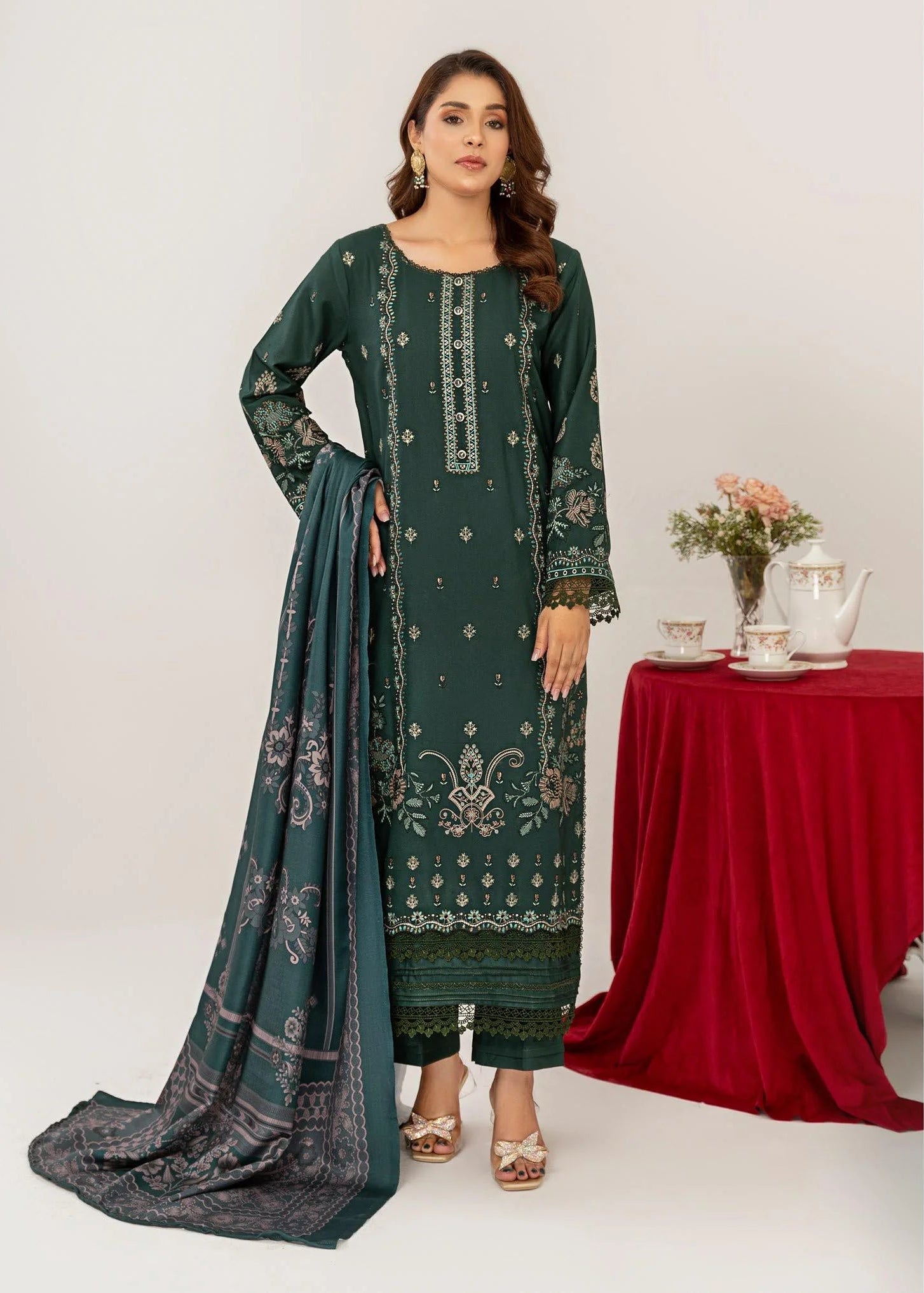Woman modeling a green embroidered outfit with a red tablecloth and flowers in the background